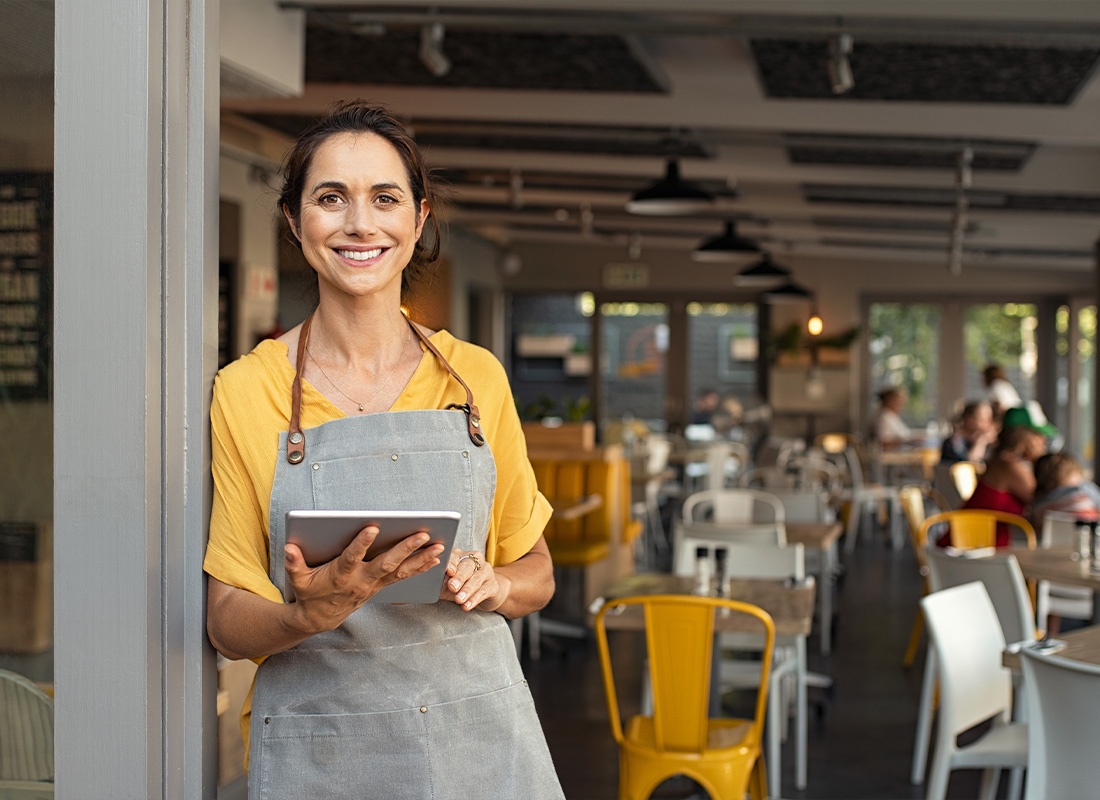 Business Insurance - Middle Aged Business Owner Standing by the Door of Shop While Holding a Tablet